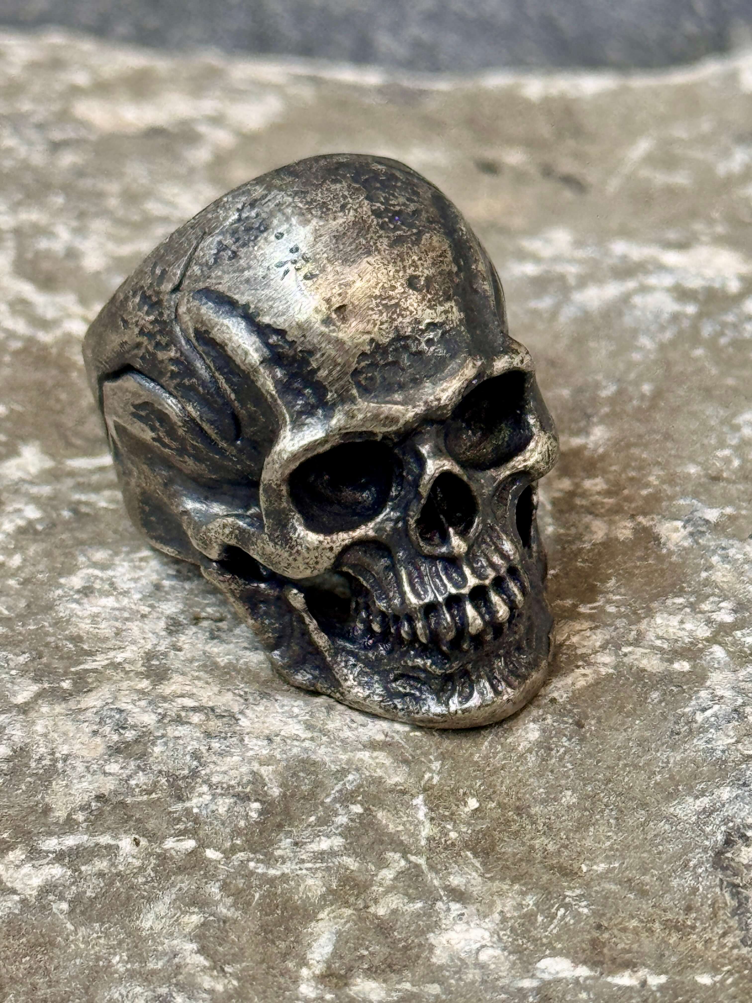 Silver skull-shaped ring on a textured stone surface